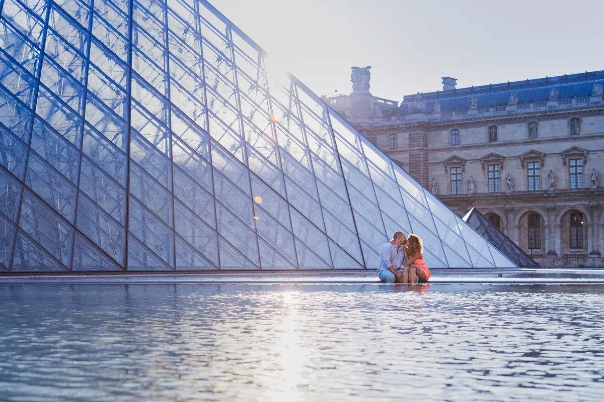 Couple photographié devant la pyramide du Louvre lors d’une séance photo au lever du jour à Paris.
