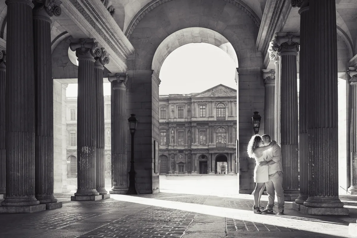 Couple enlacé sous les arcades du Louvre photographié en noir et blanc à Paris.