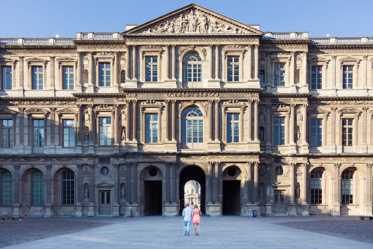 Couple photographié devant la façade du musée du Louvre au lever du soleil.