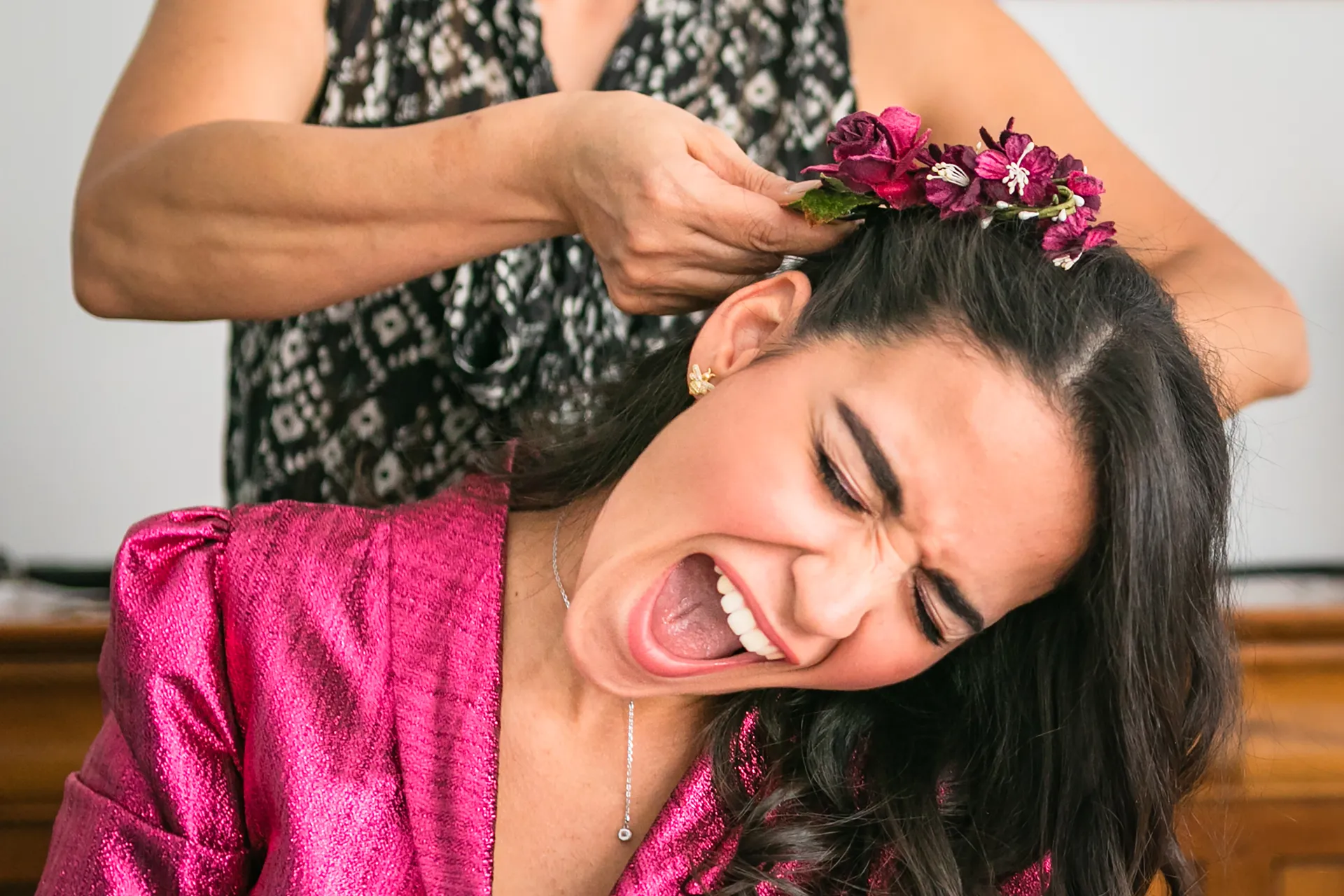 Mariée grimaçant et riant pendant que la coiffeuse fixe une couronne de fleurs dans ses cheveux, préparatifs à Paris