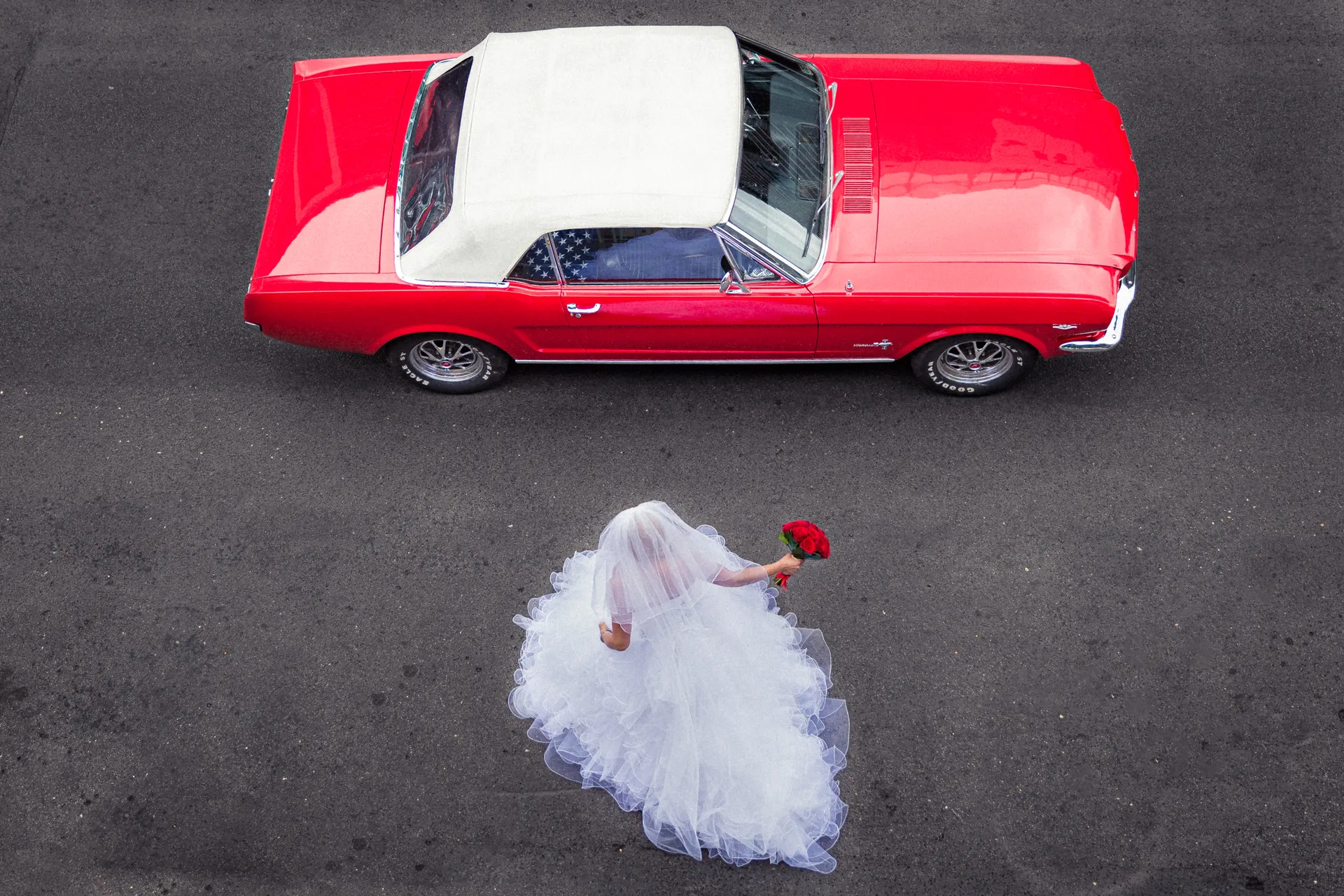 Vue aérienne de la mariée traversant l'asphalte vers une Ford Mustang rouge décapotable de 1969