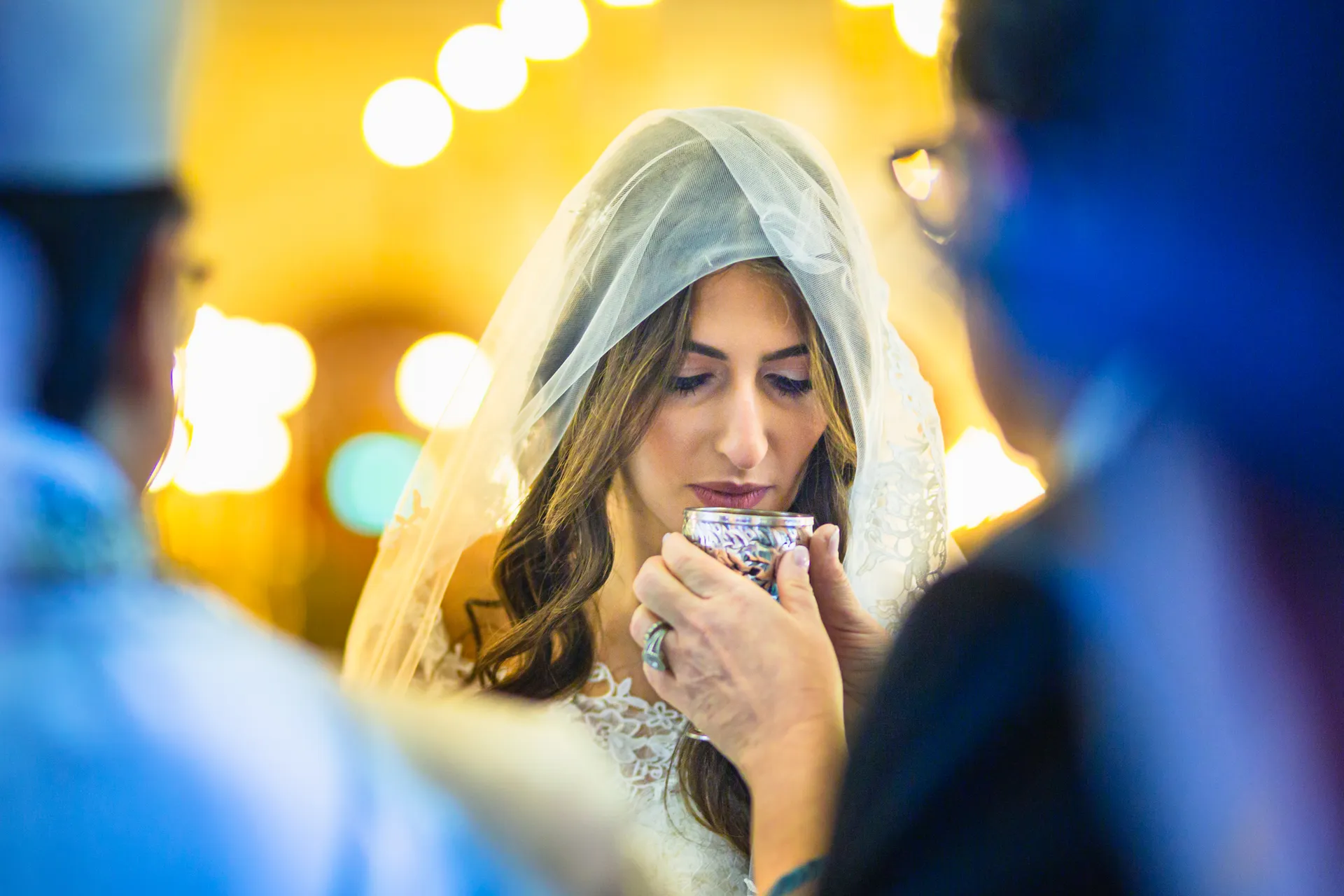 La mariée, voile sur la tête et yeux baissés, boit dans une petite coupe pendant la cérémonie de mariage.