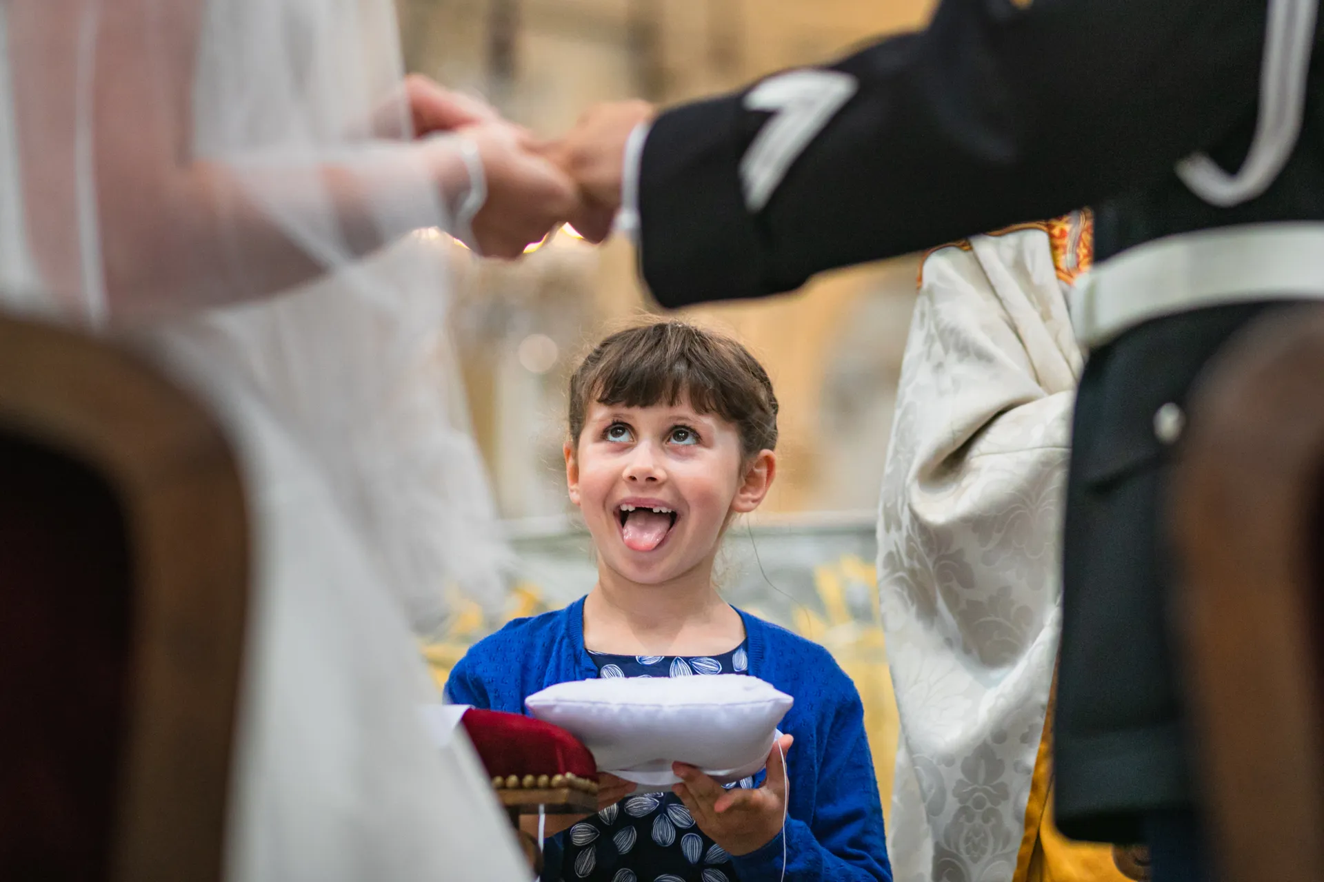 Petite fille émerveillée, langue tirée, tenant le coussin des alliances pendant l'échange des bagues des mariés, église à Paris