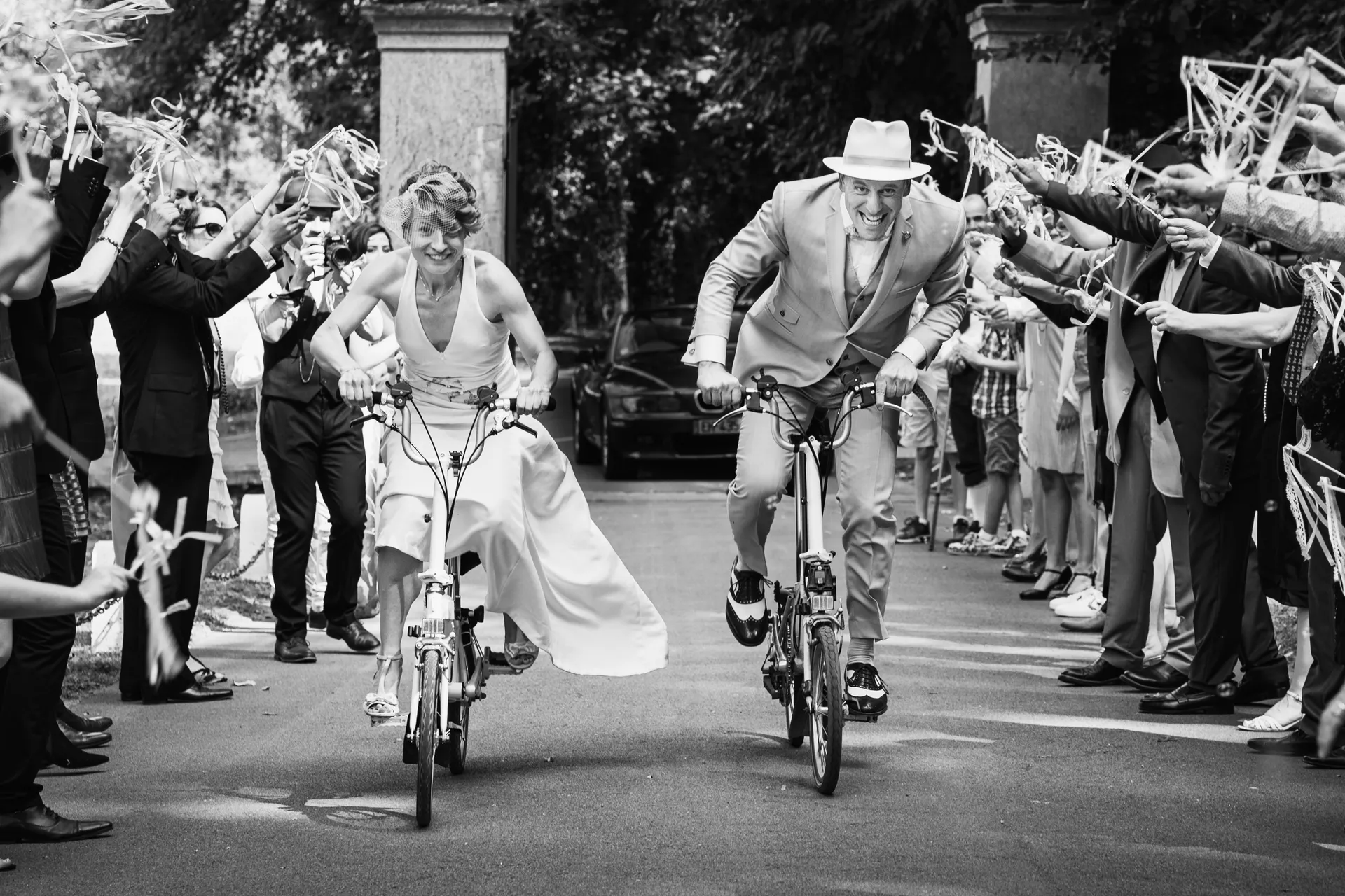 Les mariés arrivant à vélo en riant, acclamés par leurs invités en tenue années folles