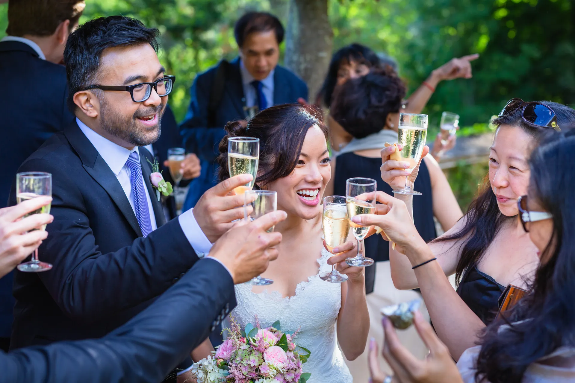 Les mariés sourient, entourés d'invités qui lèvent leurs verres pour un toast en plein air.