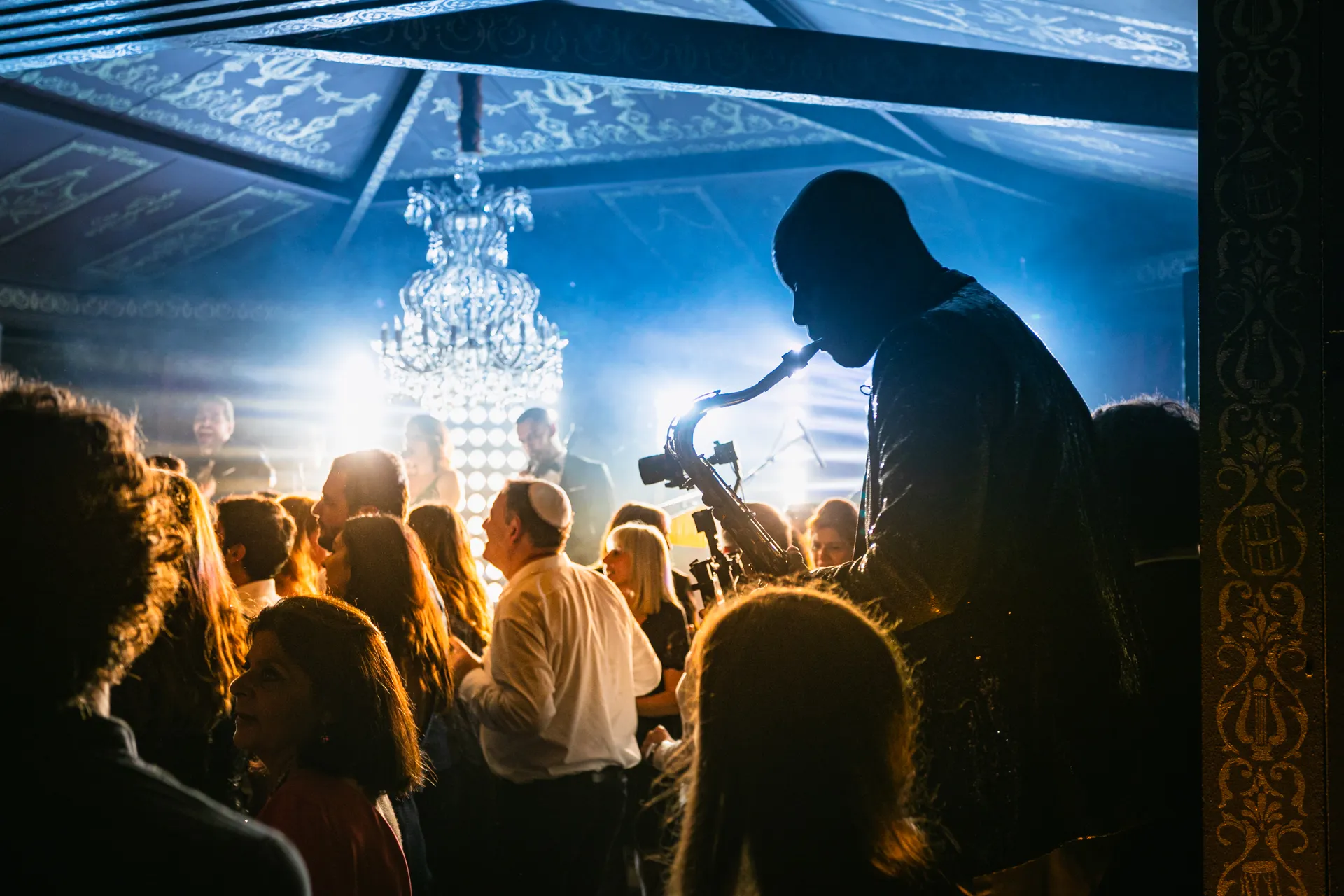 Un saxophoniste en silhouette joue parmi les invités qui dansent sous un lustre, soirée de mariage au château de Vallery.