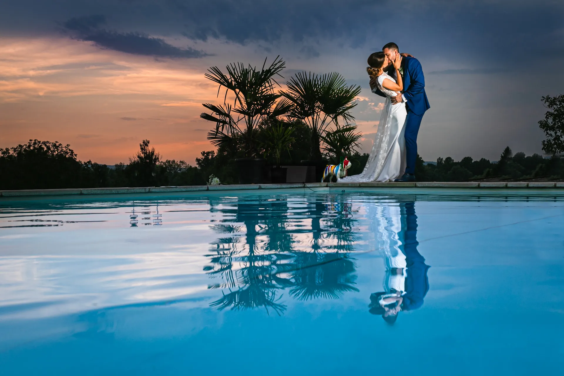 Couple de mariés s'embrassant au bord d'une piscine, reflet dans l'eau au coucher du soleil, domaine proche de Lyon