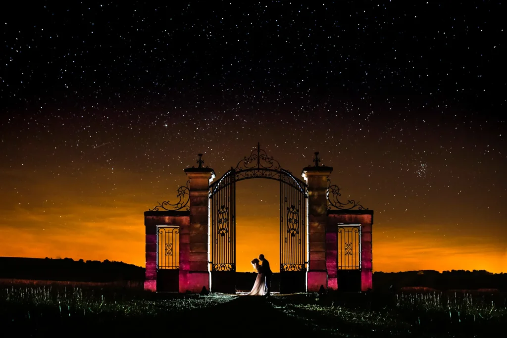 Couple de mariés enlacé sous un ciel étoilé, devant le portail illuminé de la Porte de Montesquieu en Seine-et-Marne