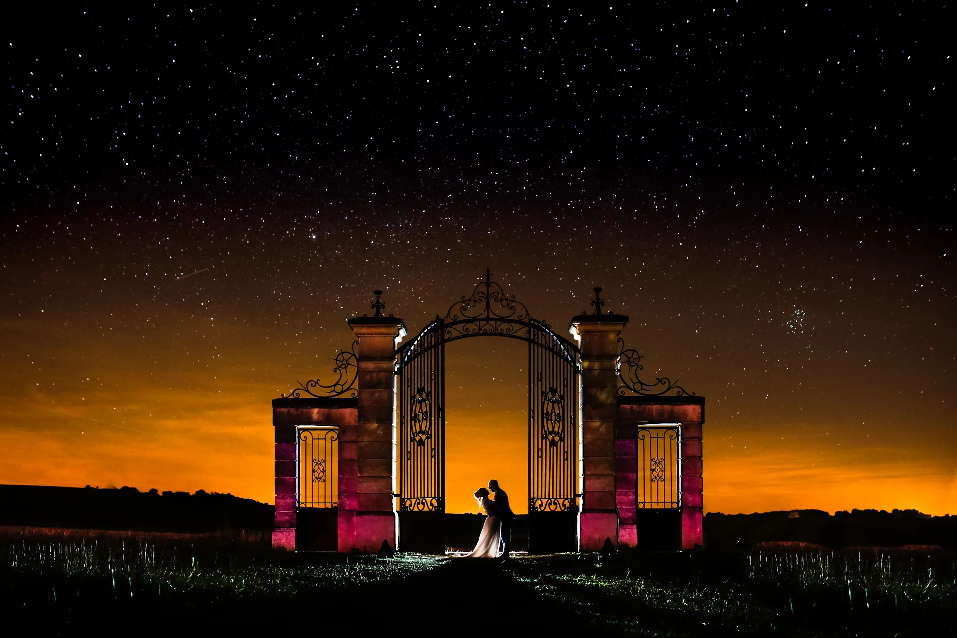 Couple de mariés enlacé sous un ciel étoilé, devant le portail illuminé de la Porte de Montesquieu en Seine-et-Marne