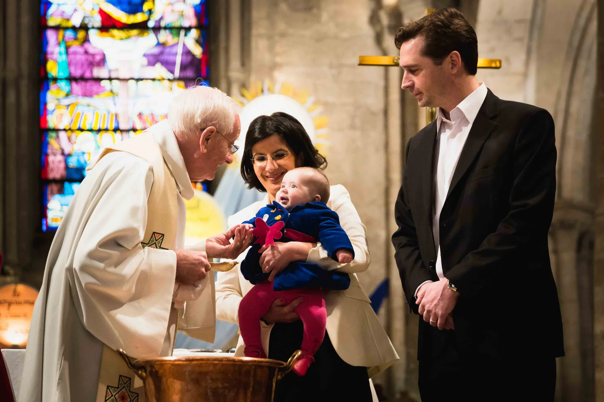 Prêtre bénissant un enfant lors d'une cérémonie de baptême entouré de ses parents