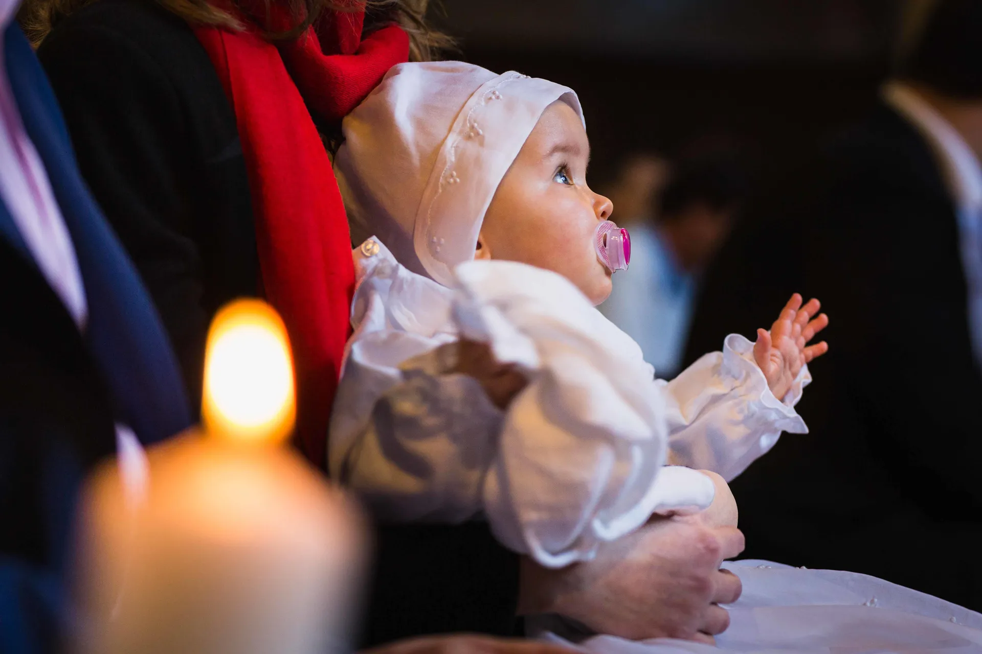 Petite fille en robe de baptême dans les bras de sa mère, attentive au prêtre, dans une église à Paris