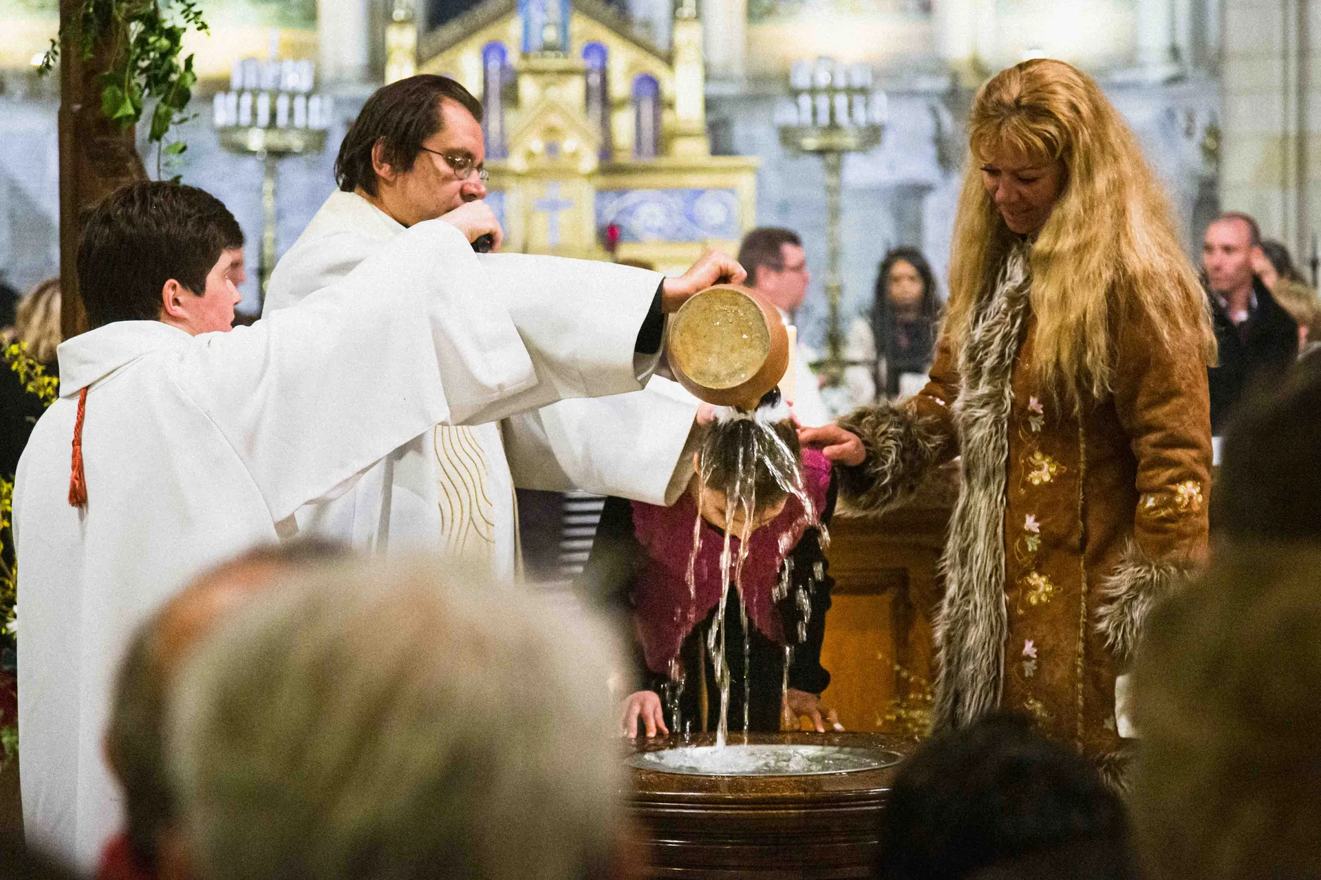 Prêtre versant l'eau bénite sur l'enfant lors de la cérémonie de baptême dans une église à Paris
