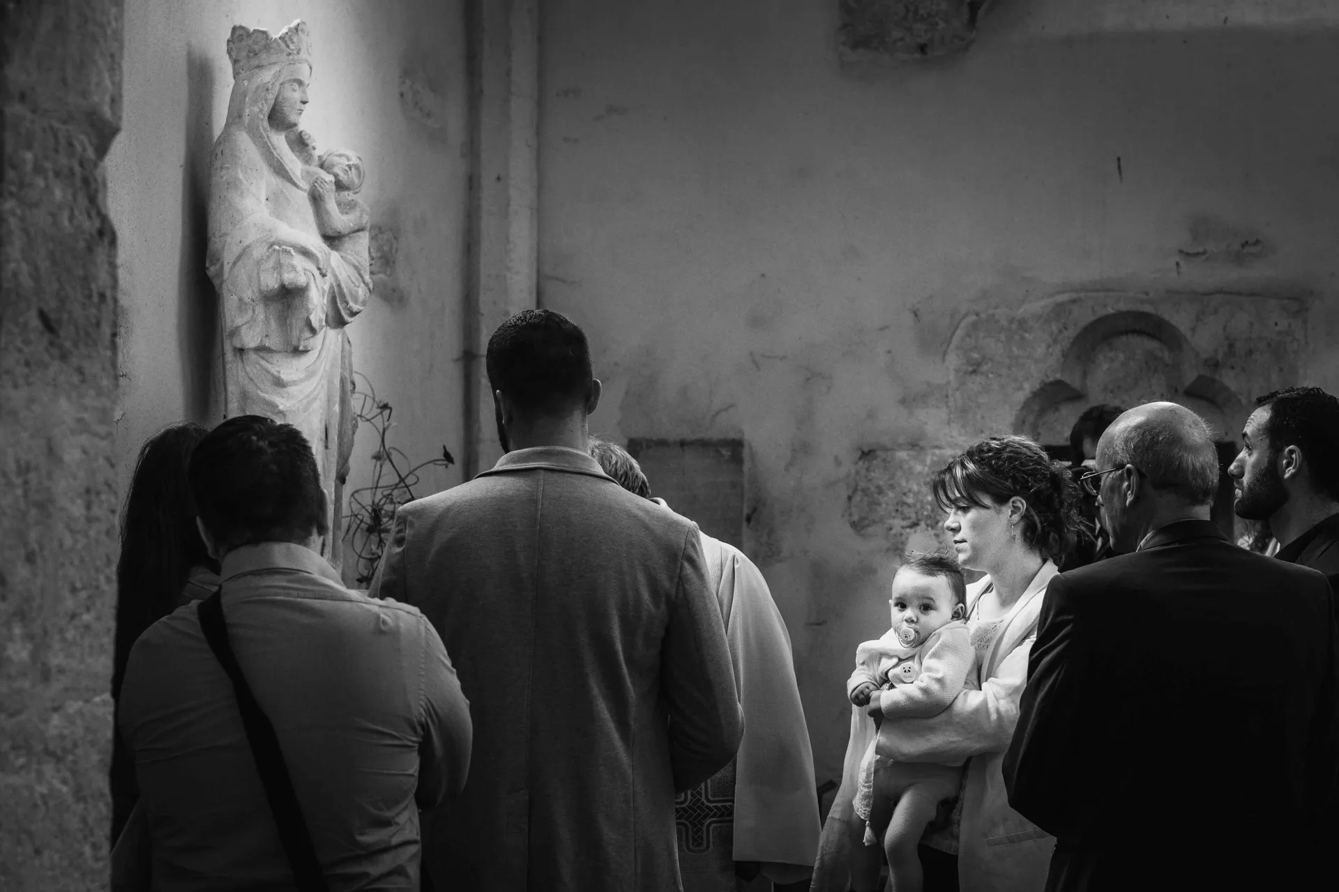 Famille de dos réunie dans une église parisienne pendant une cérémonie de baptême
