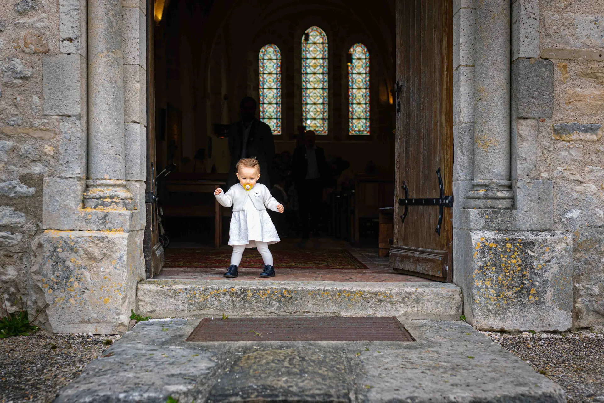 Petite fille en robe de baptême s'avançant seule sur le parvis d'une église à Paris