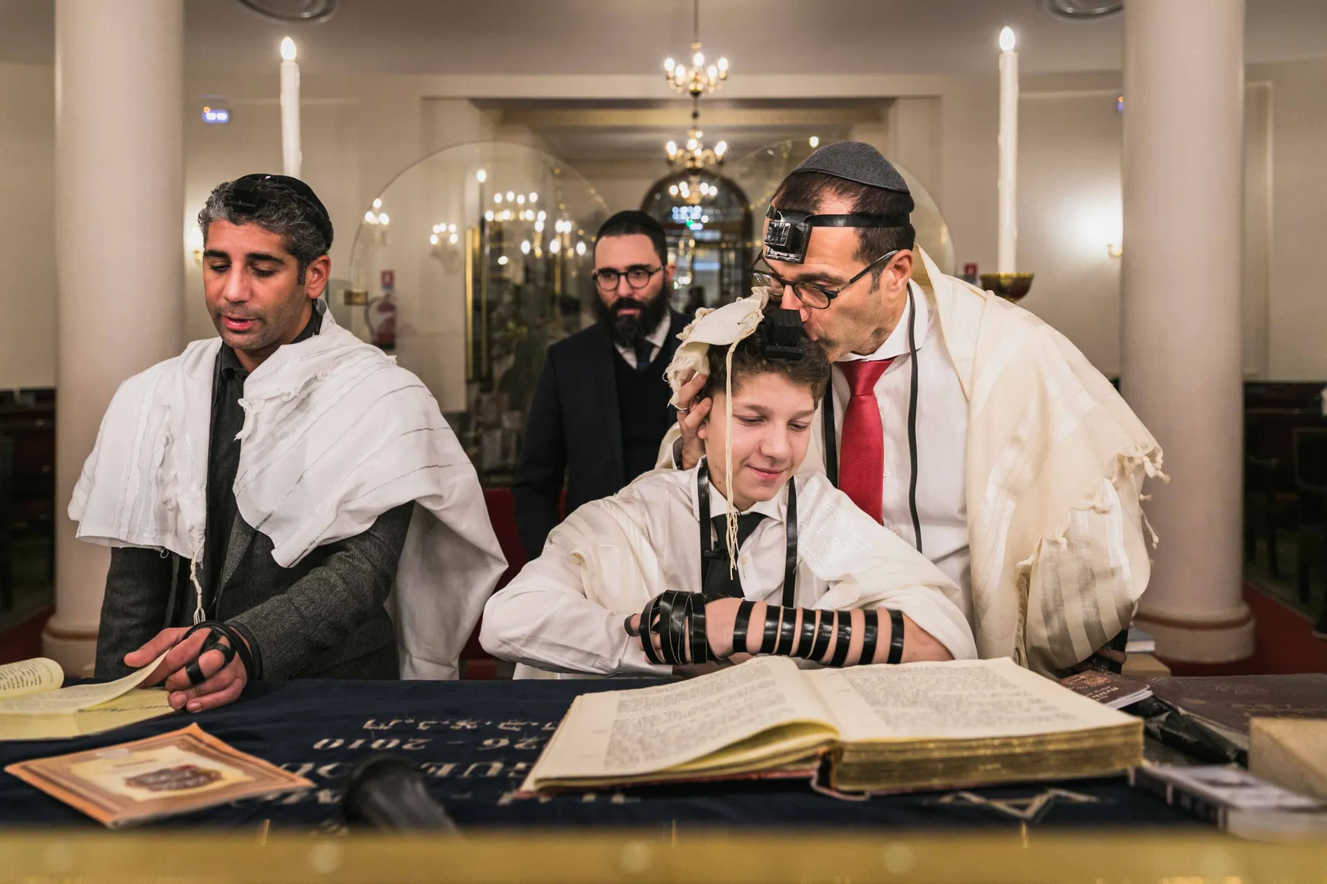Jeune Bar-Mitzvah lisant la Torah aux côtés de son père et du rabbin dans une synagogue à Paris