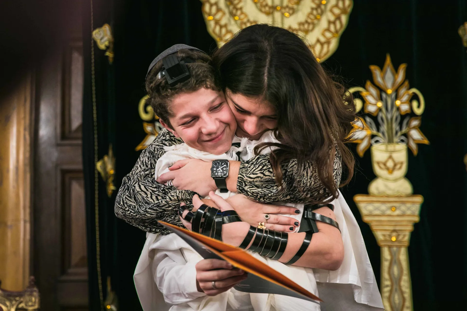 Étreinte entre le jeune garçon et sa sœur, tefillin encore au bras, lors de sa Bar-Mitzvah dans une synagogue à Paris